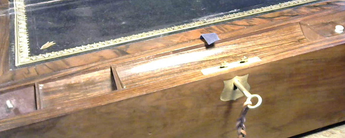 A wooden writing slope with a black leather top panel bordered by gold detailing, featuring brass hardware and a hanging key.